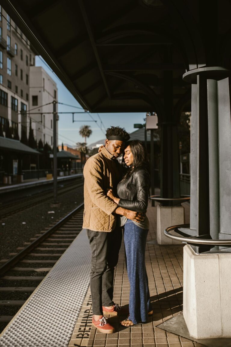 A loving couple embraces at an urban train station, symbolizing connection.
